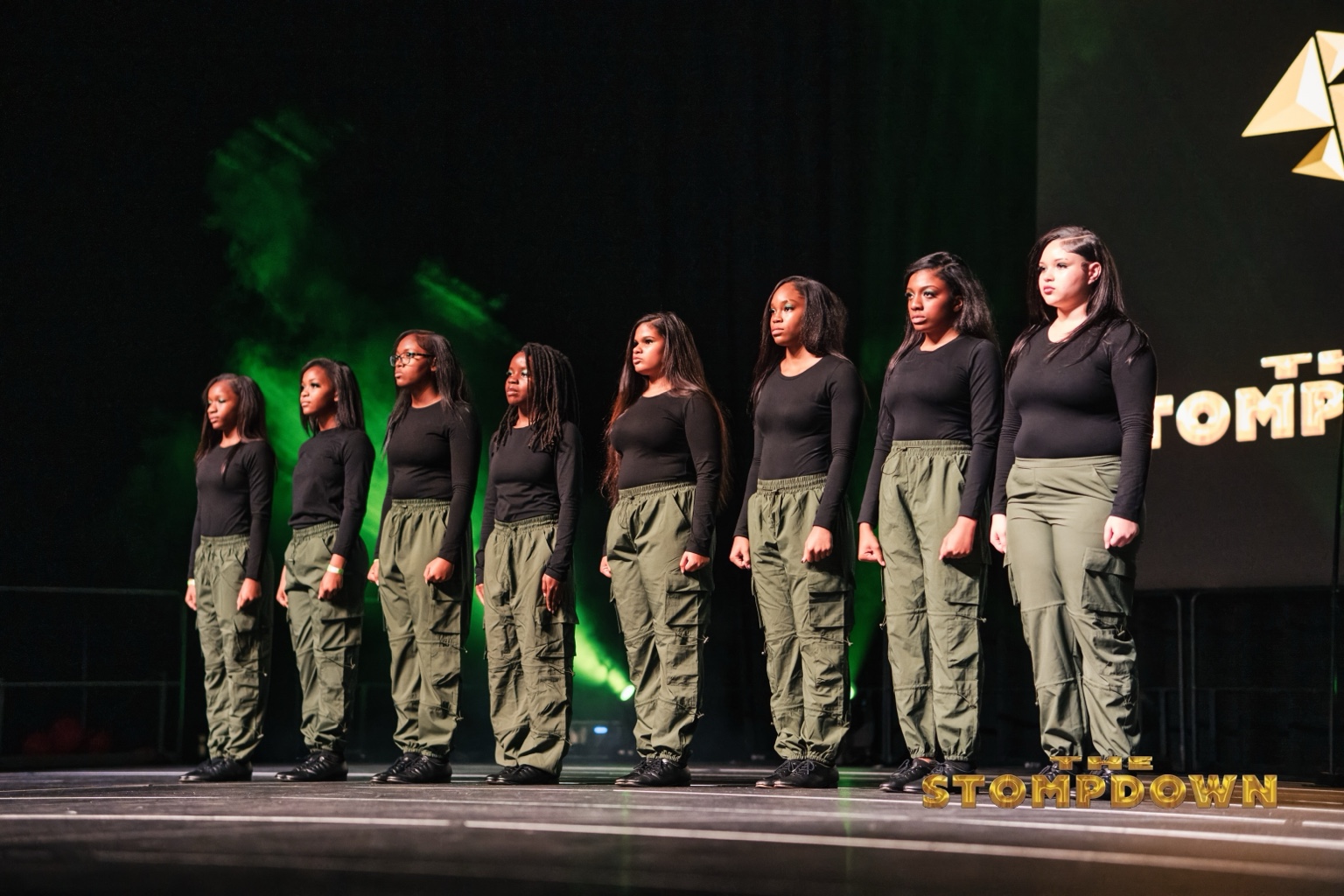 Step team lined up on stage in black and green outfits